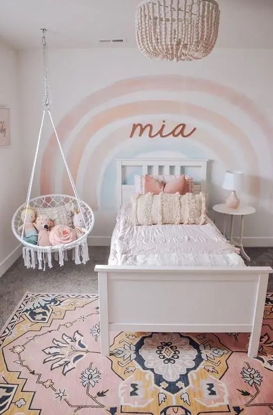 a lovely girl's room with a rainbow accent wall, a white bed and a nightstand, pendant chair, a pink printed rug is a cute and cozy space