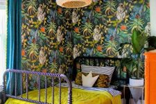 a maximalist space with bold wallpaper walls, a purple bed, a rattan lamp, an orange dresser and bright bedding is chic