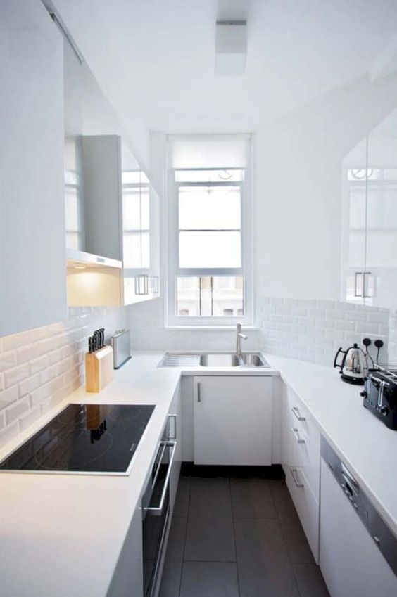 a minimalist all-white kitchen with white skinny tiles, a window, built-in appliances in black is pure chic