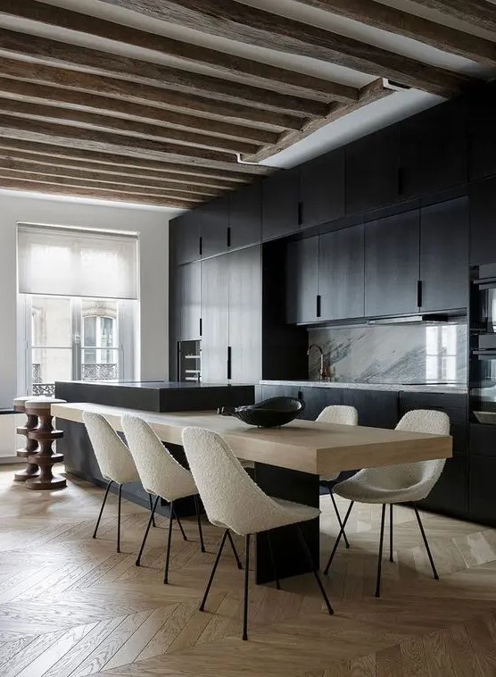 A minimalist kitchen with black cabinets, a marble backsplash, a two part kitchen island and rough wooden beams