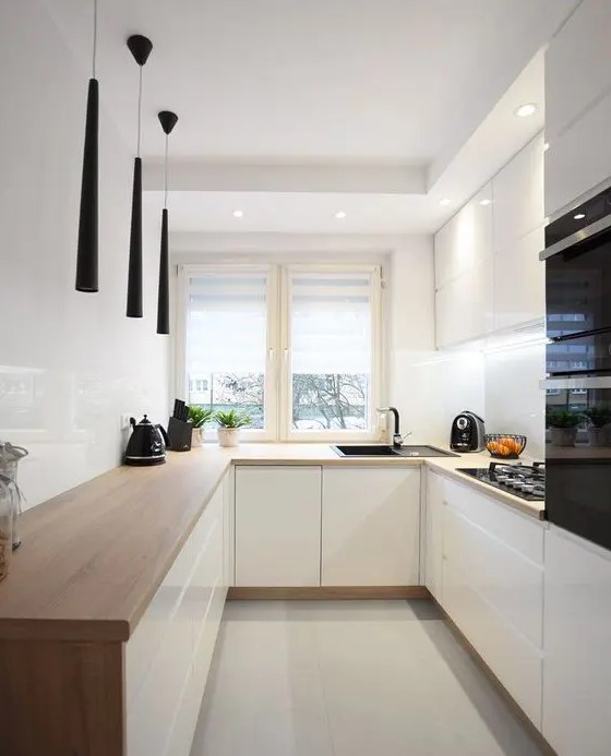 a minimalist white kitchen with butcherblock countertops, a white backsplash and catchy black pendant lamps