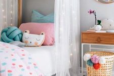 a neutral girl’s room with a house-shaped bed with pastel bedding, a nightstand, a basket with pompoms and layered rugs