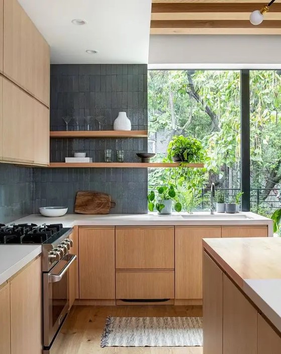 A pretty contemporary kitchen with sleek light stained cabinetry, grey skinny tiles, open shelves and a large window with greenery views