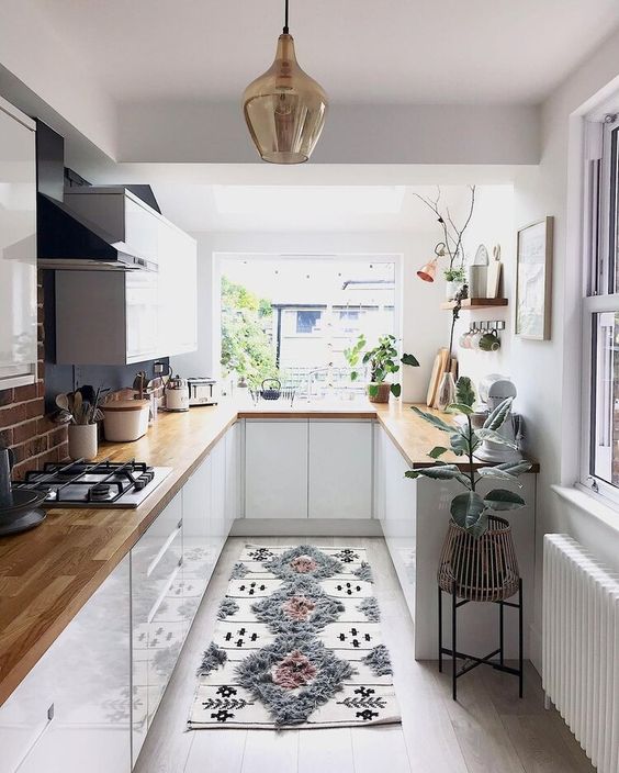 a pretty small kitchen with white cabinets, butcherblock coutnertops, potted plants and a printed rug