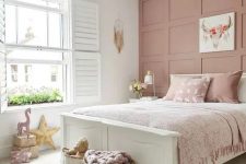 a relaxed and delicate girl’s room with a dusty pink wall, a white bed with dusty pink bedding, artwork and pillows is cute