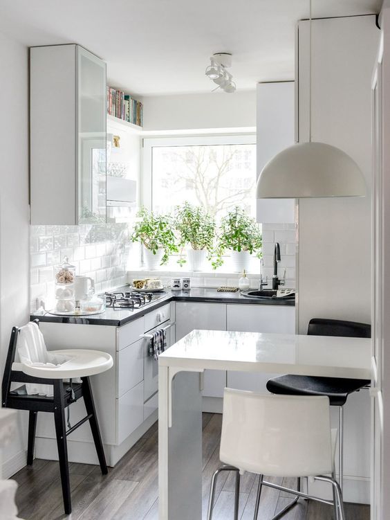 a small Scandinavian kitchen with white glossy cabinets, black countertops, a bar countertop, a pendant lamp and stools