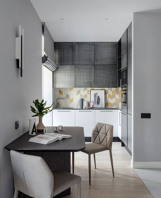 A small contemporary kitchen in grey and white, with a bright tile backsplash, built in appliances and a dining zone next to it