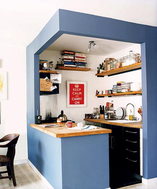a small kitchen cube with blue walls, black cabinets, open shelves and butcherblock countertops is super cool