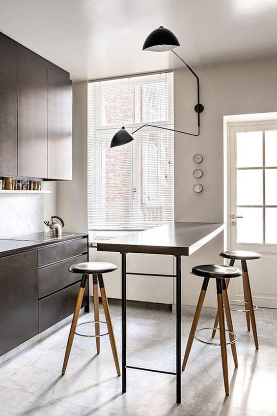 a small kitchen with sleek brown cabinetry, a tall bar countertop and tall stools plus a cool sconce