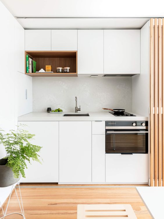 a small minimalist kitchen in white, with a white tile backsplash and a white stone countertop that can be hidden with a screen