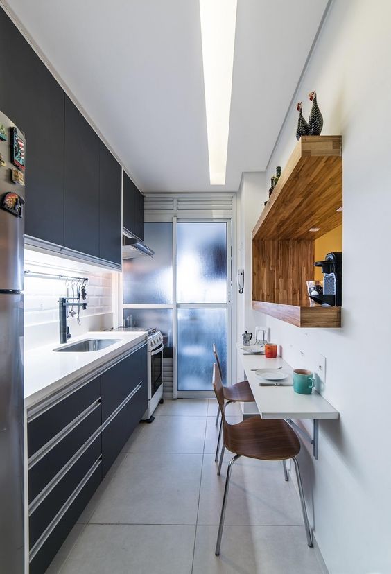 a small sleek black kitchen with a thick white stone countertop, a white tile backsplash, a built-in shelf with a coffee machine and a bar table