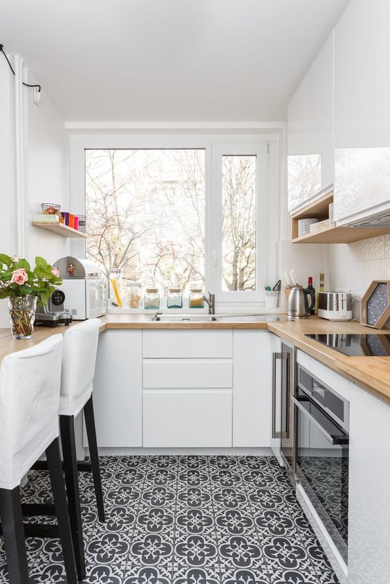 a small white kitchen with butcherblock countertops, white stools and a window with a view