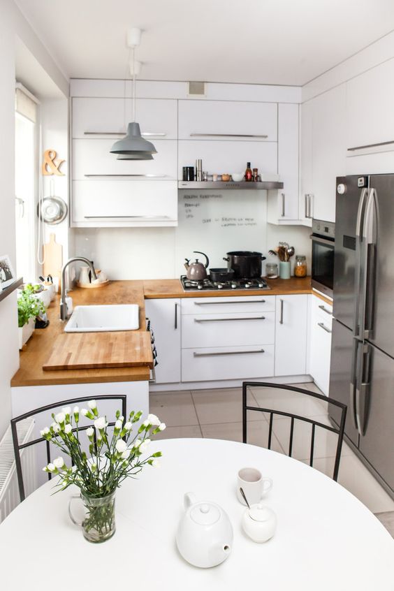 a small white kitchen with butcherblock coutnertops, stainless steel appliances and a round table and chairs