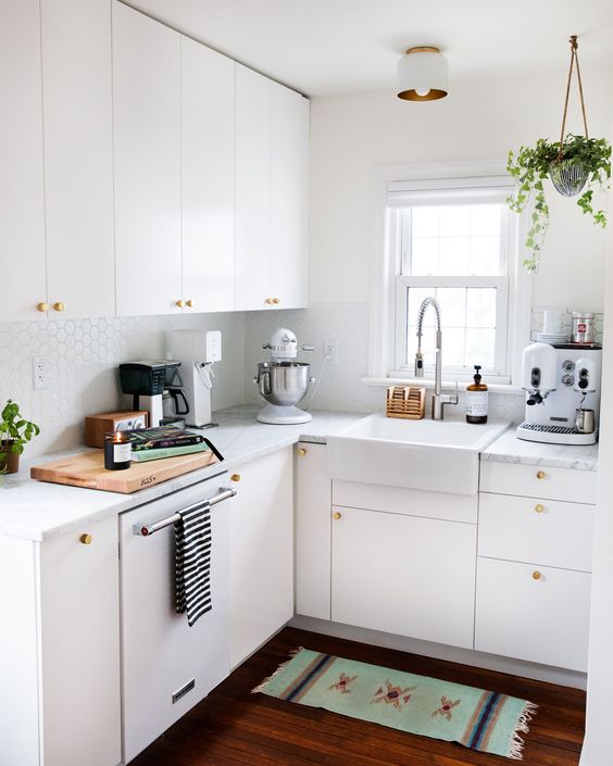 a small white kitchen with penny tiles, with white stone countertops, gold knobs and potted greenery