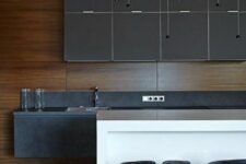 a super stylish minimalist kitchen with matte grey cabinets, stone countertops, a white kitchen island plus black stools