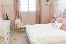 a sweet pink girl’s room with paneling, a bed with white and pink bedding, pink polka dot curtains, a white dresser