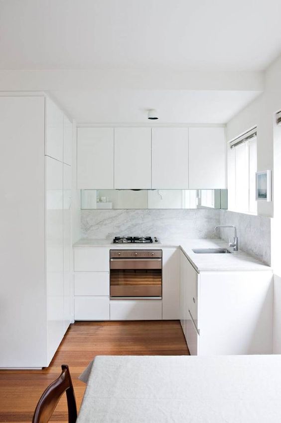 a tiny minimalist kitchen with a white backsplash and countertops, a mirror touch and an eating space