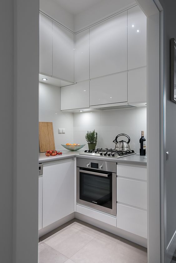 A tiny white sleek kitchen with built in lights, metal countertops, built in appliances is chic and cool