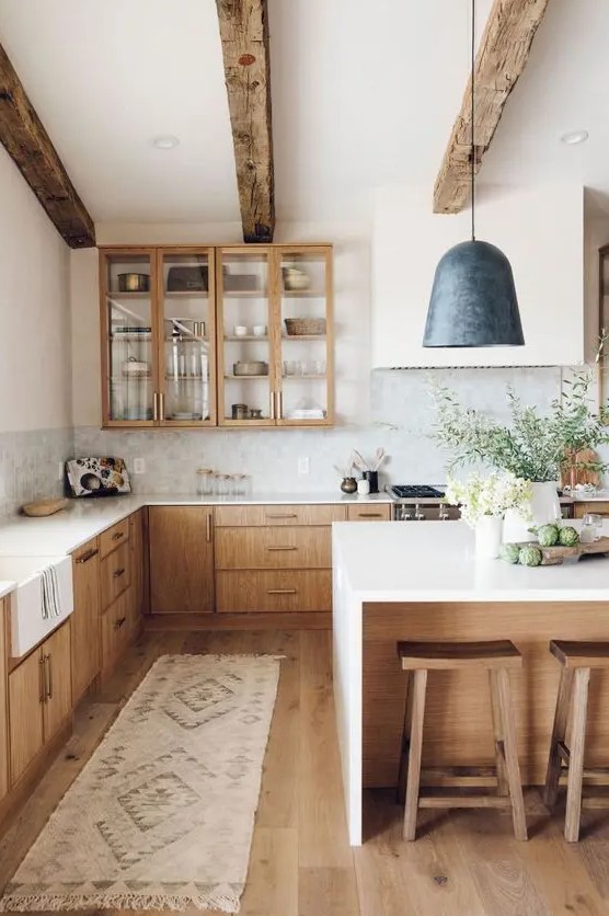 A welcoming modern farmhouse kitchen with light colored cabinets, wooden beams and stools that warm up the space