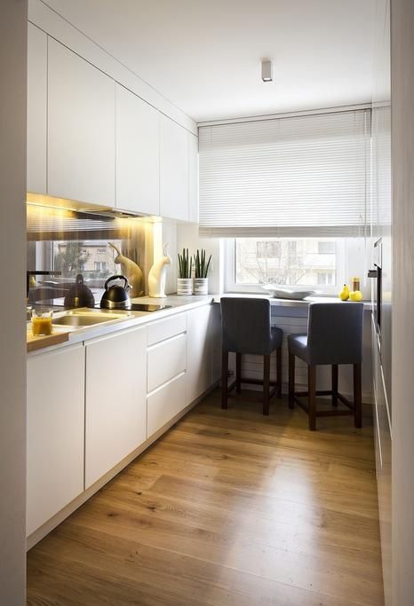 A white minimalist kitchen with a glossy backsplash, built in lights, a windowsill breakfats bar
