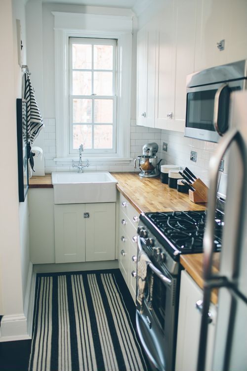 a white modern kitchen with butcherblock countertops, a white tile backsplash, a striped rug and neutral handles