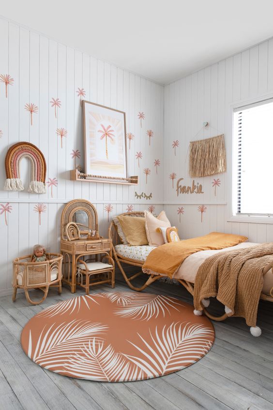An earthy tone girl's room with paneling, rattan furniutre, warm colored bedding, a printed rug, fringe and some hangings on the wall