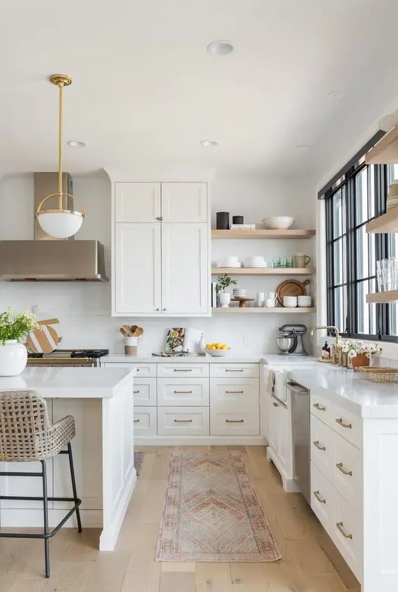 An elegant white L shaped kitchen with a kitchen island, open shelves, catchy lamps and brass touches