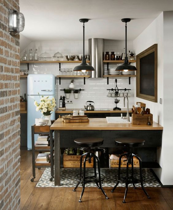 an industrial kitchen with blakc cabinetry, butcherblock countertops, a white tile backsplash and pendant lamps