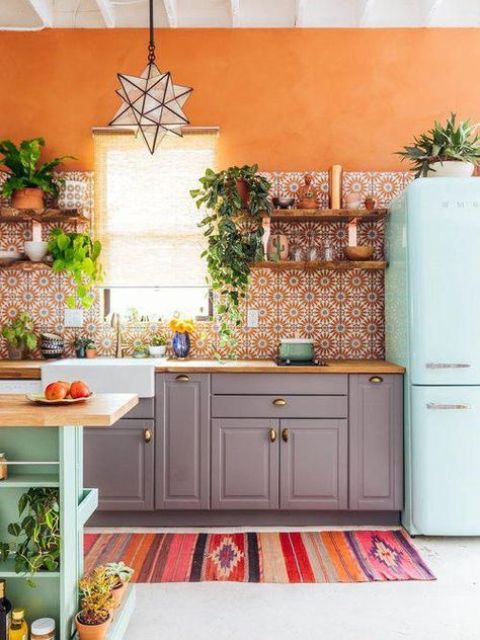 a bold kitchen with grey cabinets, an orange printed tile backsplash, a mint blue fridge and a kitchen island plus a colorful rug