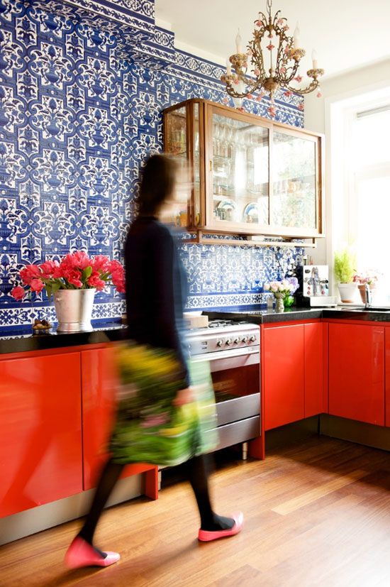 a bold red kitchen with a blue patterned tile wall, a glass cabinet and a refined and chic chandelier over the space