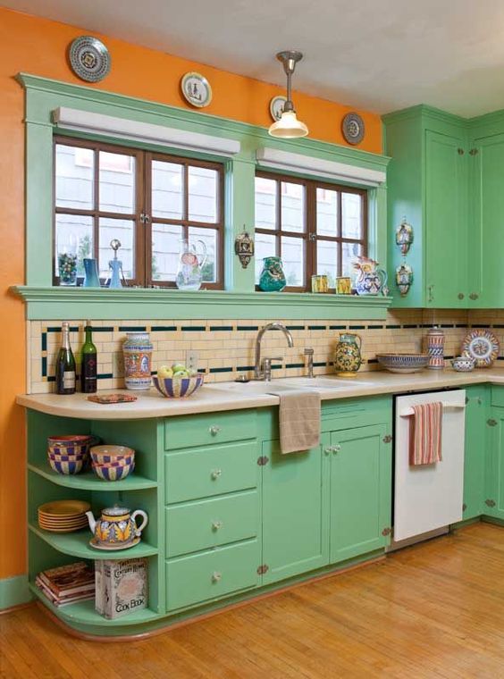 a bold retro ktichen in green, with orange walls, a neutral and black tile backsplash and decorative plates on the wall