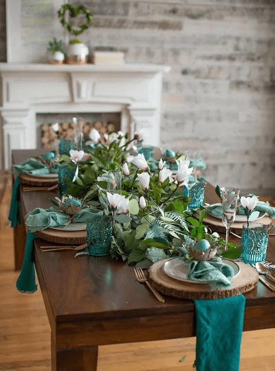 a botanical Easter tablescape with teal and green napkins, greenery, pink blooms, nests with green eggs