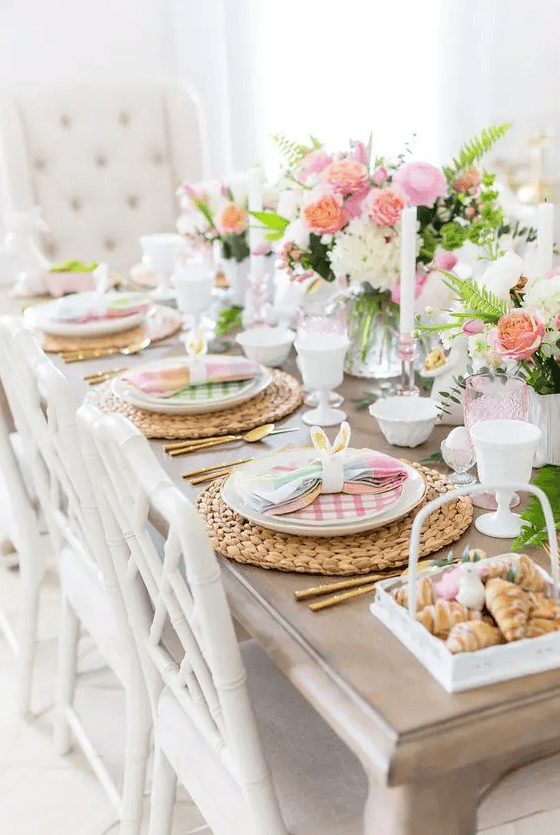 a bright Easter table with woven placemats, colorful napkins and plates, bold pink blooms and glasses plus bunny ears and eggs