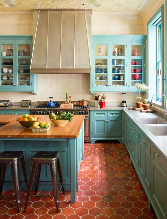 a bright blue kitchen with terracotta tile on the floor, a large vintage hood, butcher block countertops and a patterned ceiling
