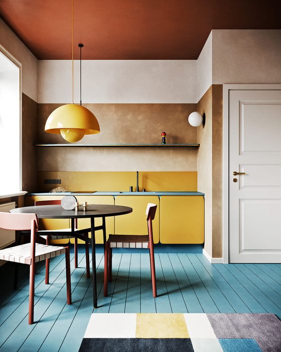 a bright modern kitchen with yellow cabinets and a pendant lamp, a blue floor and blue countertops plus a geometric rug