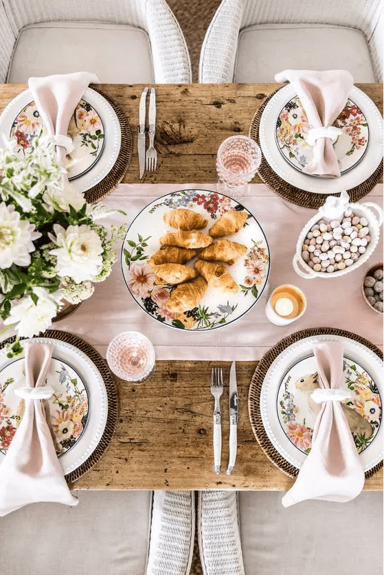 a chic pastel Easter tablescape with a pink runner and napkins, floral plates, woven chargers, white blooms and pink glasses
