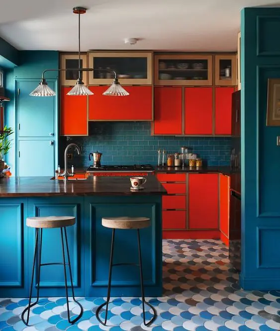 a colorful kitchen with bright red cabinets, navy cabinets, walls and a backsplasj plus a retro pendant lamp and a scallop tile floor
