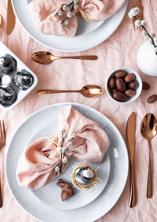 a delicate blush Easter tablescape with pink linens, marble eggs, willow and rose gold cutlery