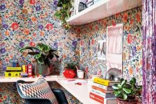 a jaw-dropping home office nook covered with bright floral wallpaper, white floating shelves and a pink floating desk, lots of books and potted plants