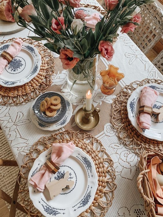 a modern farmhouse tablescape with a doily tablecloth, woven placemts, printed plates, blush napkins, fresh blooms and candles
