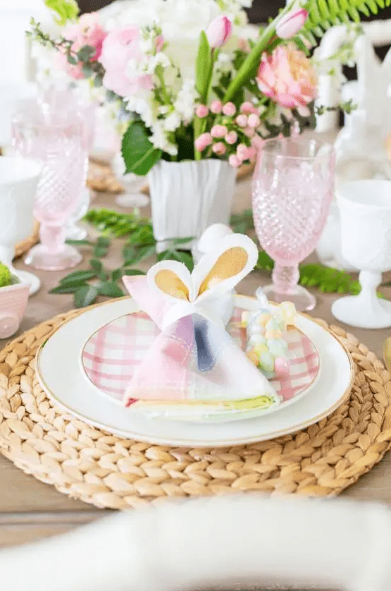 a pastel Easter tablescape with woven chargers, plaid plates, colorful napkins, pink and white blooms and pink glasses