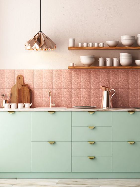 a pretty contemporary kitchen with mint cabinetry and gold handles, patterned and textural pink tiles, a copper geometric pendant lamp