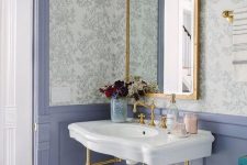 a pretty powder room with floral wallpaper, blue panels, a console sink, a mirror in a gilded frame, sconces and white appliances