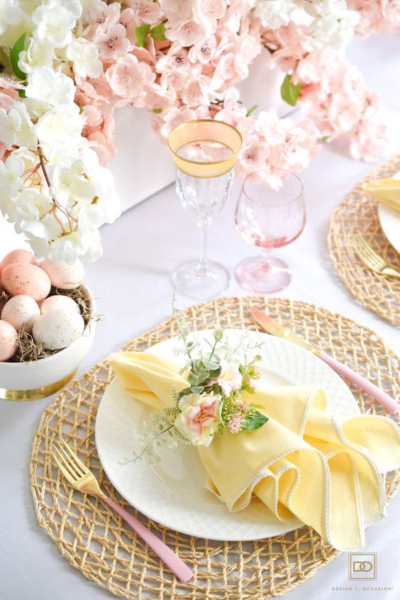 a refined and fresh Easter tablescape with faux cherry blossom, woven placemats, yellow napkins with floral rings and speckled eggs