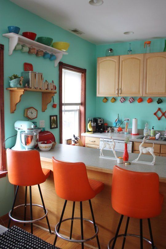 a retro blue ktichen with orange stools and colorful tableware plus mugs is a very stylish and bold space