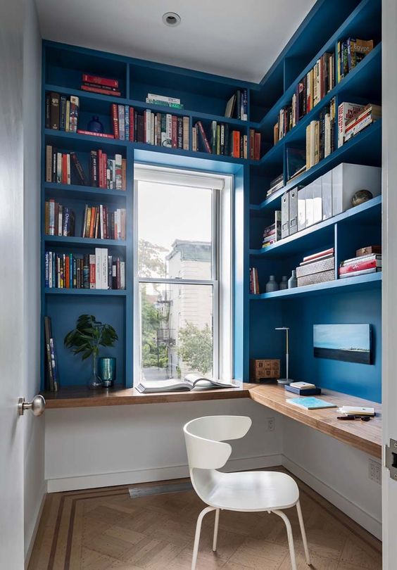 a small bright home office done in blue, with built-in bookshelves and a desk, a small window and a white chair is a cool idea for tight spaces