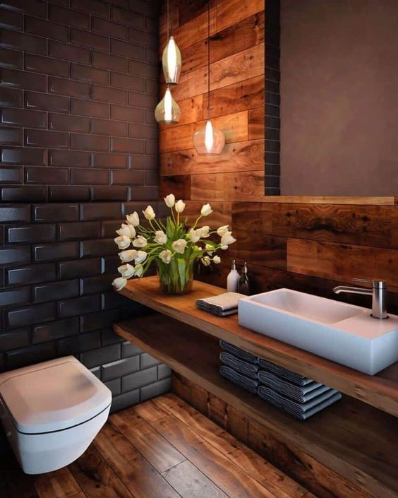 a stylish modern powder room with tiles, wood cladding the wall and floor, a floating vanity and a cluster of pendant lamps