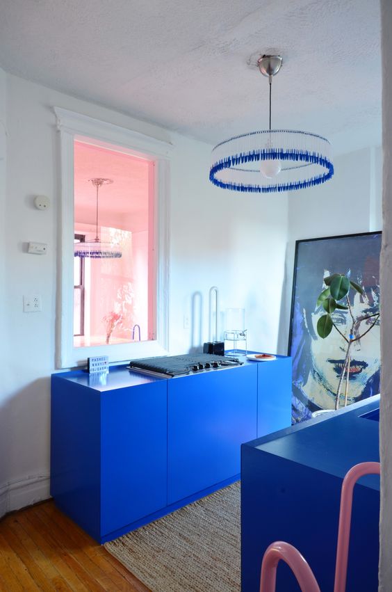 a super bold blue, yet small kitchen with not many cabinets, a statement artwork and a bright blue chandelier