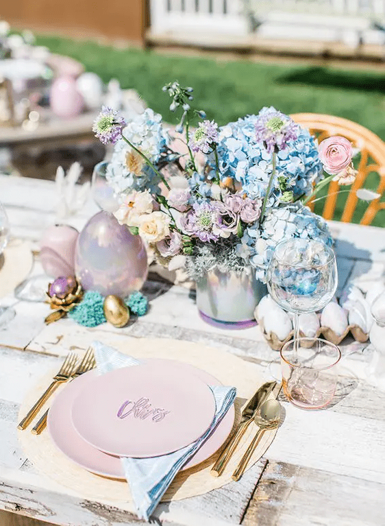 A watercolor Easter tablescape with pink plates, blue napkins, lilac, blush and blue florals and pastel colored eggs