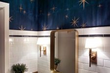 a whimsy powder room with white tiles, navy walls and a ceiling, gold stars, gold fixtures and a gold frame mirror